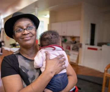 A woman with a hat and glasses holds a small baby